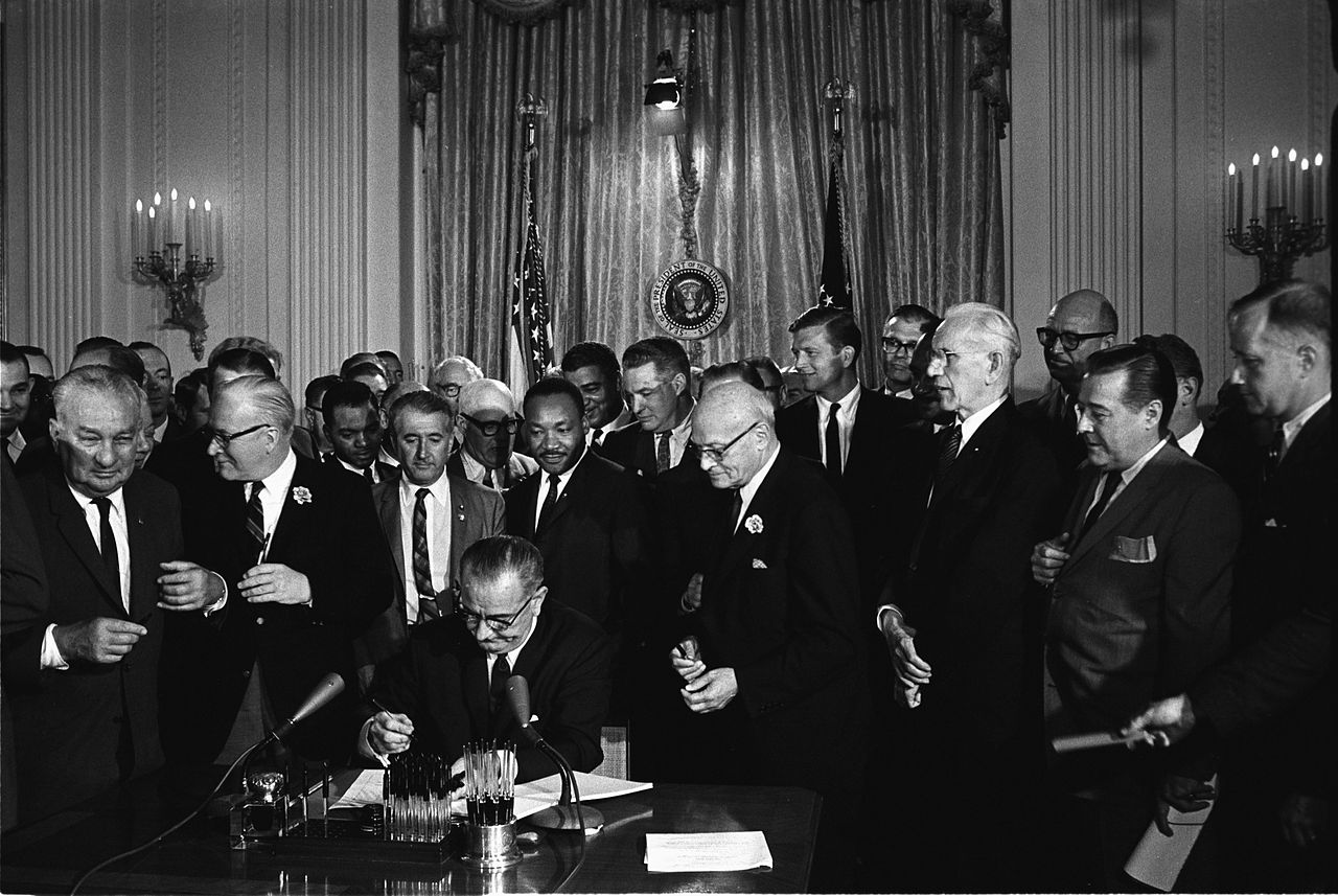 Pictured: President Lyndon B. Johnson signs the 1964 Civil Rights Act as Martin Luther King, Jr. and other leaders look on. Photo by Cecil Stoughton, White House Press Office.